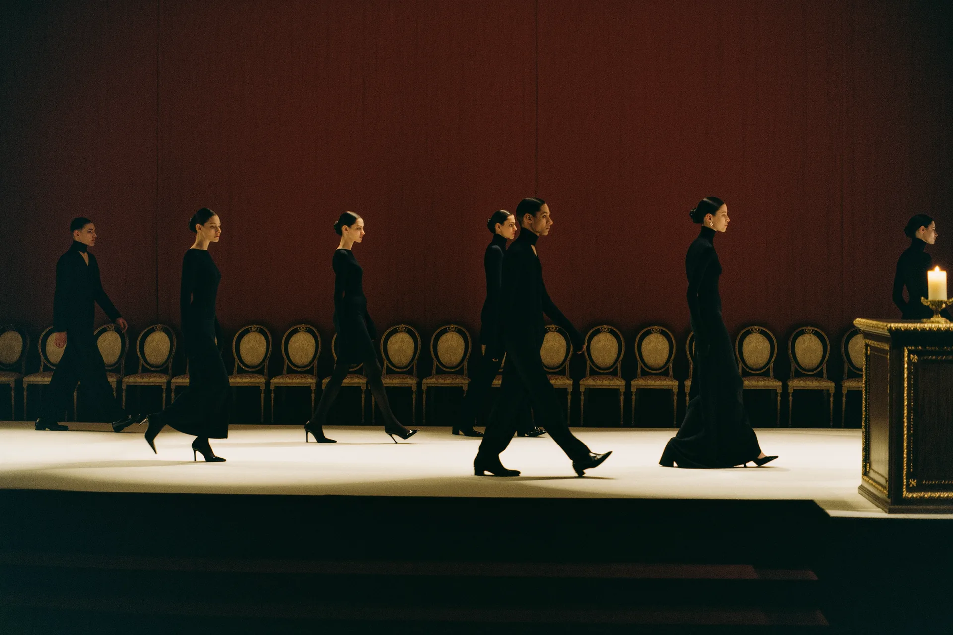 Silhouettes en cadence sur un podium éclairé, rangée de sièges en pénombre