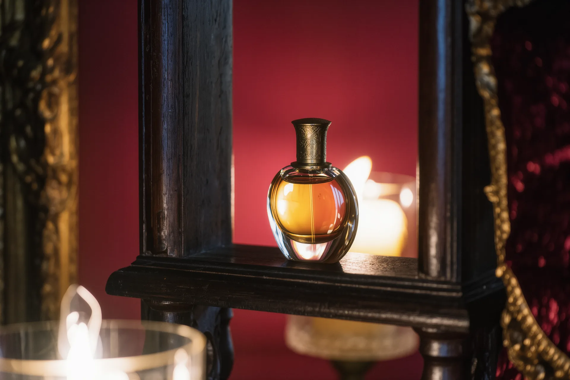 Flacon de parfum ambré photographié à contre-jour sur une étagère en bois sombre