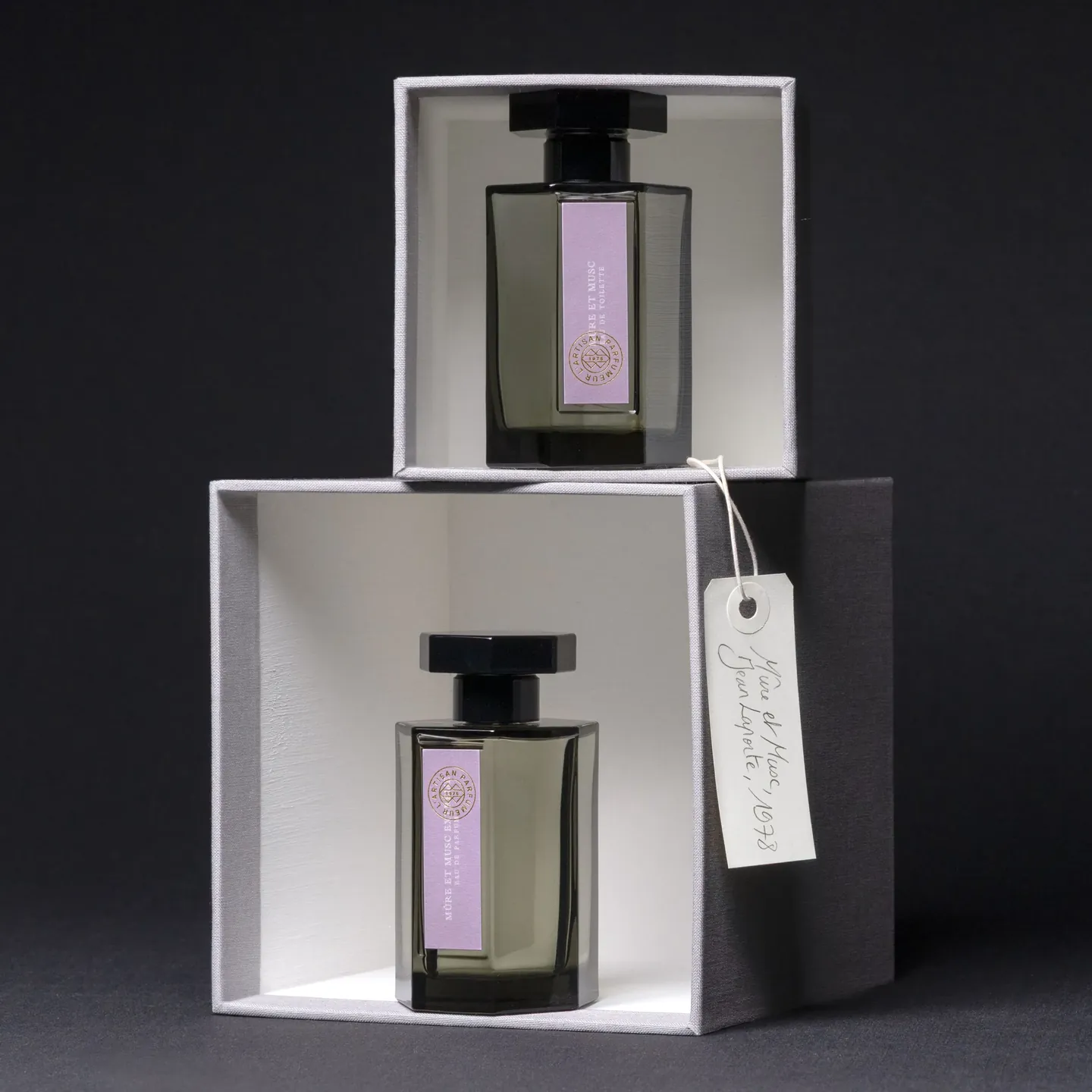 Deux flacons de L'Artisan Parfumeur dans leurs coffrets ouverts, une étiquette nouée au flacon du haut