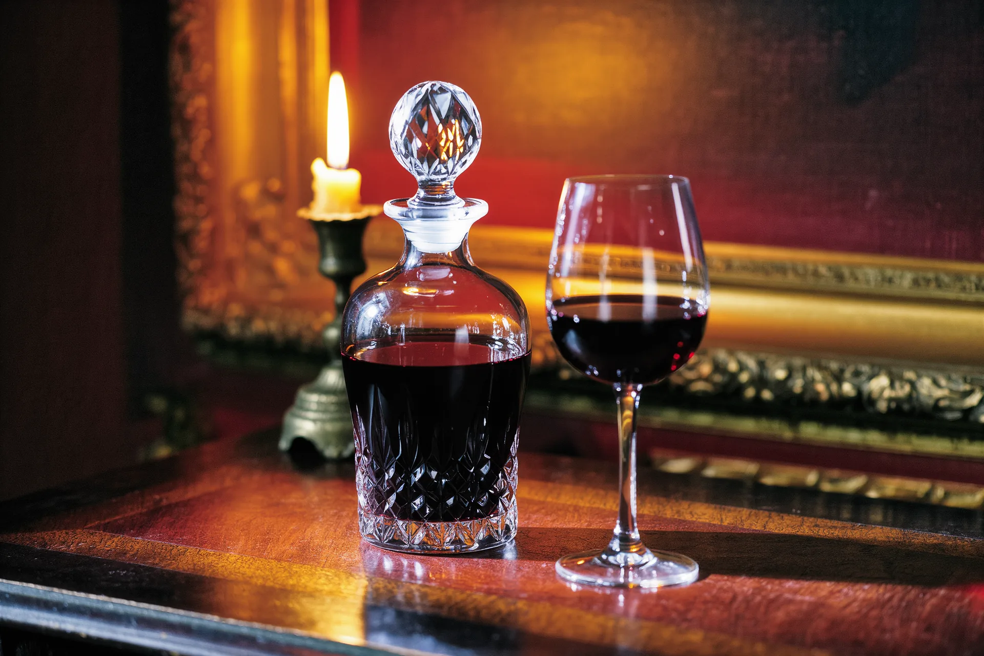 Carafe en cristal remplie de vin rouge, posée près d'un verre sur une table sombre