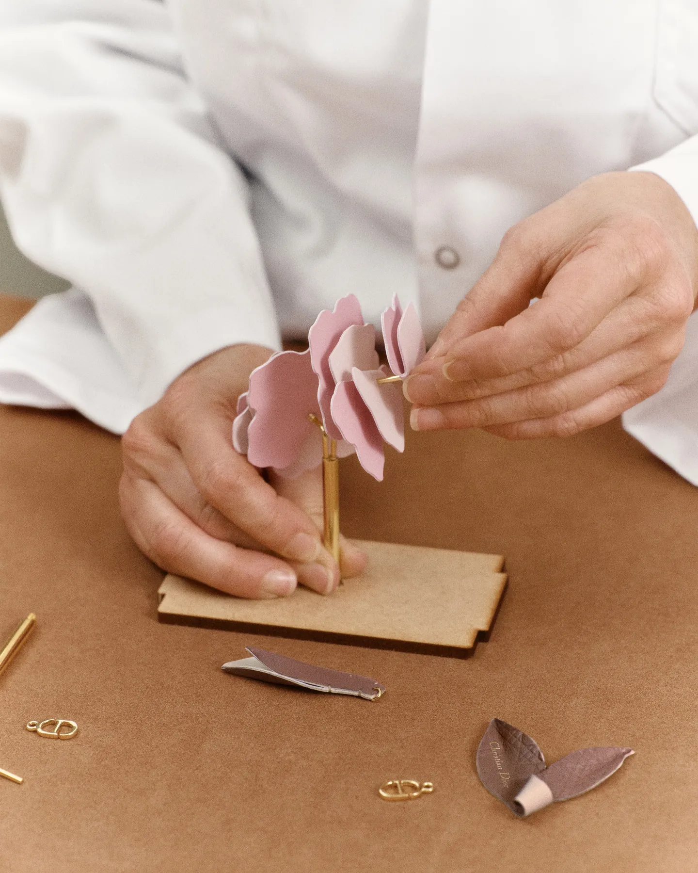 Mains assemblant pétale par pétale la rose en cuir du flacon Parfums Christian Dior sur un établi