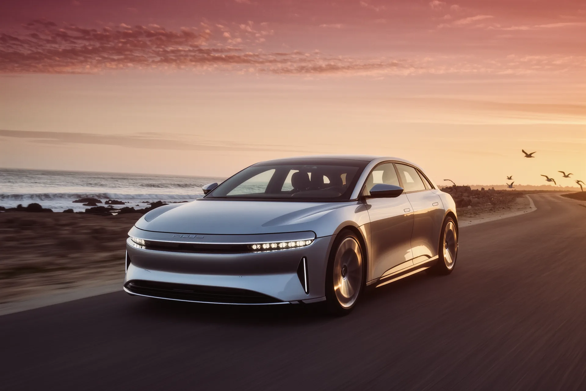 Coupé de grand tourisme électrique argenté filant sur une route côtière au crépuscule