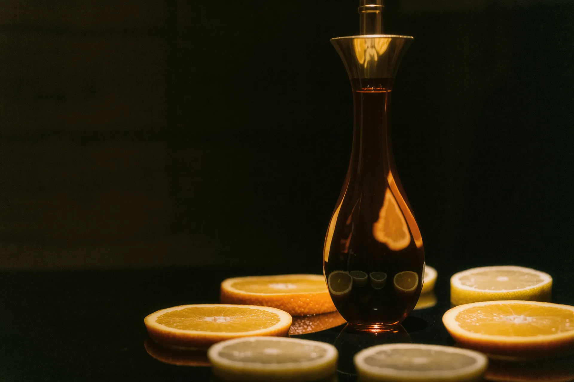 Flacon ambré de sérum vitamine C entouré de tranches d'agrumes en clair-obscur.