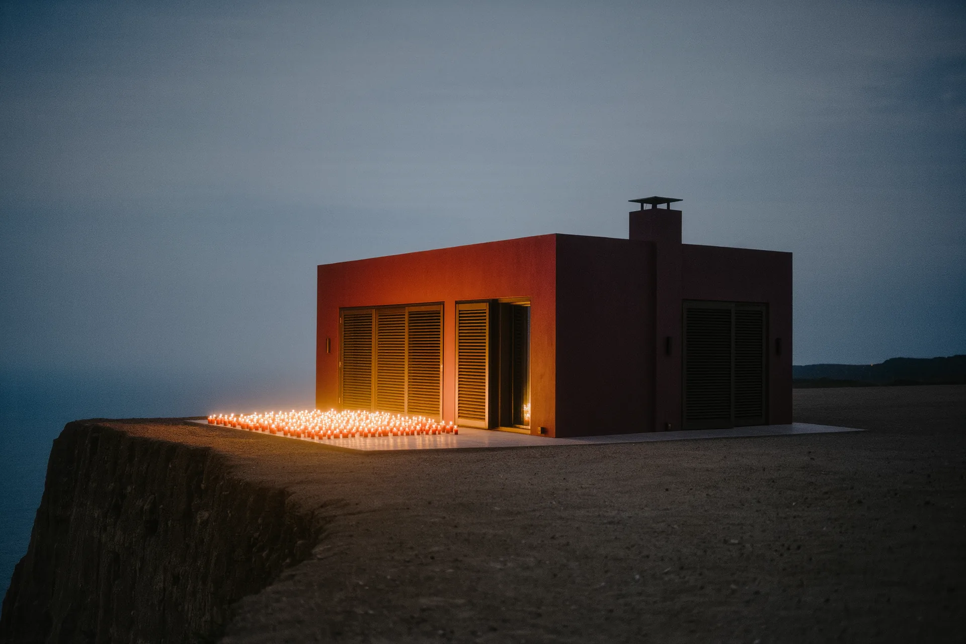 Villa isolée en bord de falaise, volets clos, aucune enseigne visible, lumière rasante du soir