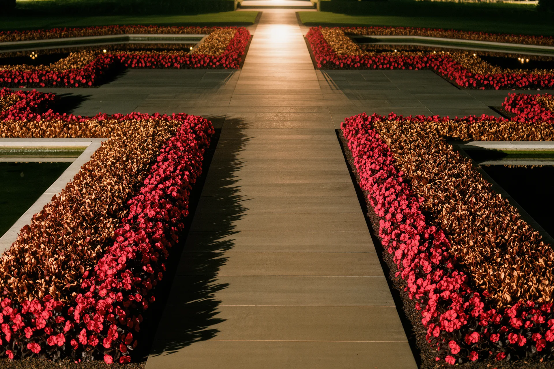 Allée centrale d'un jardin à la française bordée de parterres géométriques et de bassins symétriques.