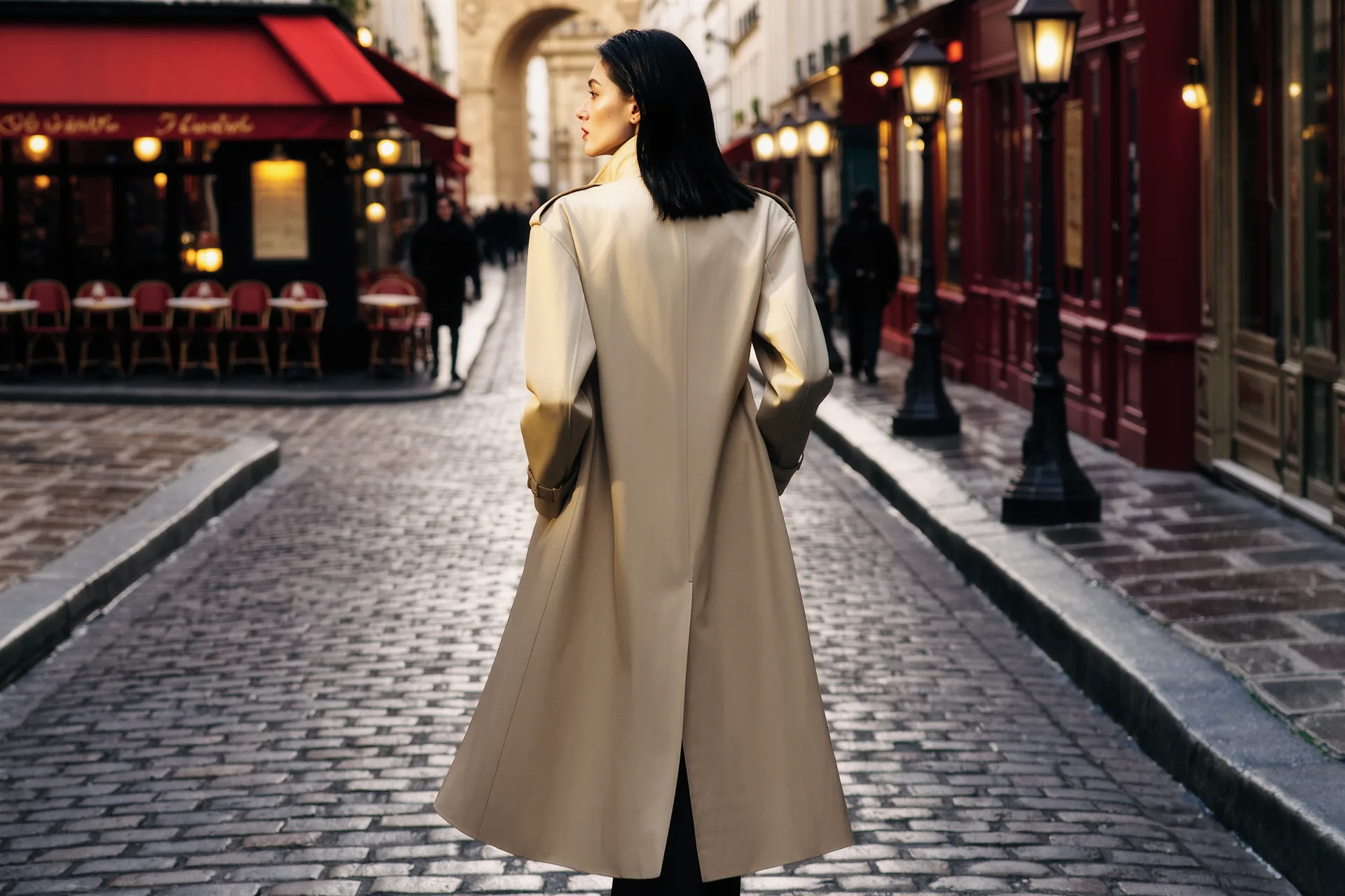 Trench-coat beige photographié de dos dans une rue pavée, lumière froide d'après-midi